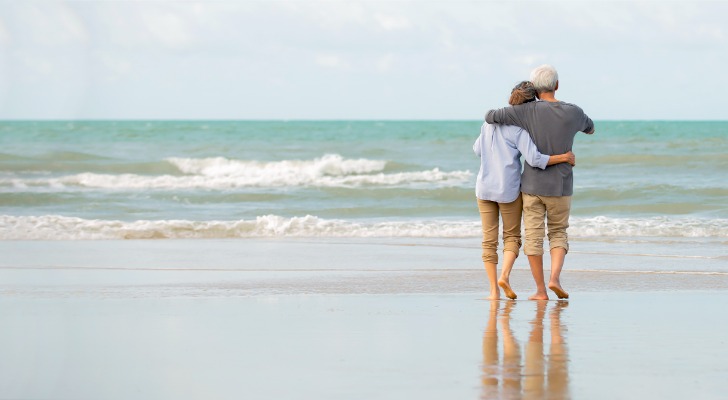 A retired couple enjoys a walk on the beach.